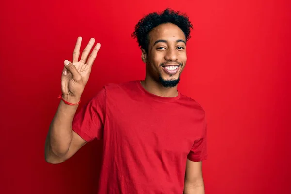 自信と幸せ笑顔ながら カジュアルな赤いTシャツを着て指の数3を示すと指摘髭を生やした若いアフリカ系アメリカ人男性 — ストック写真