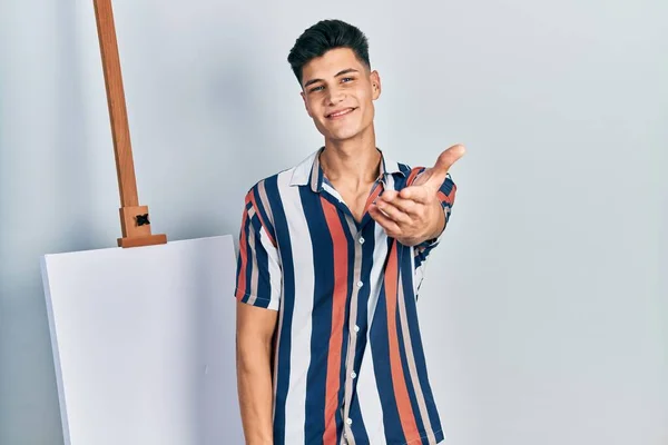 Молодий Іспаномовний Чоловік Стоїть Поруч Порожнім Полотном Усміхнений Доброзичливий Пропонує — стокове фото