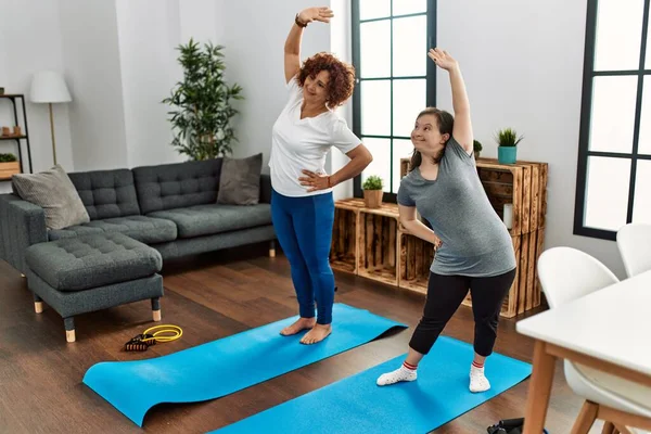 Mature mother and down syndrome daughter doing exercise at home. Stretching at the living room