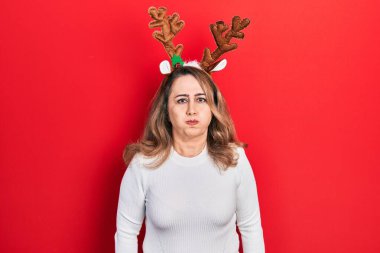 Orta yaşlı beyaz bir kadın şirin Noel geyiği boynuzları takıyor komik yüzlü yanakları şişiriyor. Havayla şişmiş ağız, çılgın bir ifade.. 