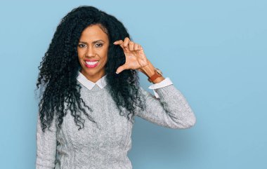 Orta yaşlı Afro-Amerikalı kadın, günlük kıyafetler giymiş, gülümseyen ve kendine güvenen, el hareketleriyle küçük beden işareti yapan, parmaklarıyla işaret eden ve kamerayla bakan. ölçüm kavramı. 