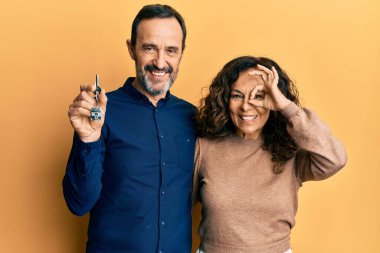 Orta yaşlı İspanyol çift yeni evlerinin anahtarlarını tutarken gülümsüyor mutlu mesut, el pençe divan duruyorlar. 