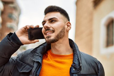 Yakışıklı, sakallı, mutlu, kendine güvenen, kışlık palto giymiş telefonda konuşan bir İspanyol.