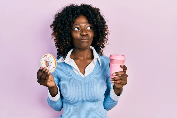 Młoda Afroamerykanka Jedząca Pączki Pijąca Kawę Uśmiechnięta Patrząca Bok Patrząca — Zdjęcie stockowe