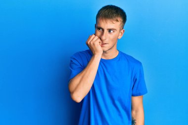 Günlük mavi tişört giyen genç beyaz adam gergin ve gergin görünüyor. Ağzı tırnak ısıran elleri var. anksiyete. 