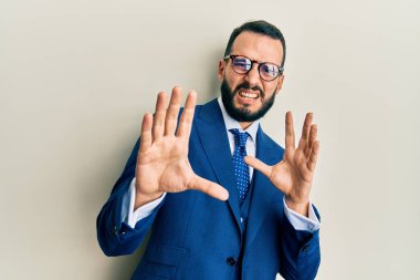 Sakallı, takım elbiseli ve kravatlı bir genç, tiksindirici bir yüz ifadesi takınıyor ve tiksindirici bir ifade takınıyor. Eller havada. 