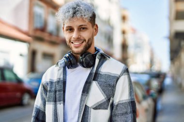 Şehirde kulaklık takarak mutlu gülümseyen genç İspanyol adam..