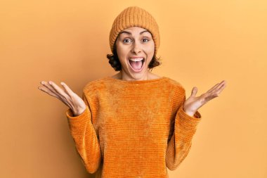 Genç esmer kadın yün şapka ve kışlık süveter giyerek zaferi kutluyor. Gülümsüyor ve ellerini kaldırarak kazanan ifade. 