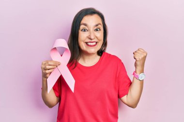 Orta yaşlı İspanyol kadın pembe kanser kurdelesi tutuyor gururla haykırıyor, zaferi kutluyor ve başarıyı kollarını kaldırarak kutluyor. 