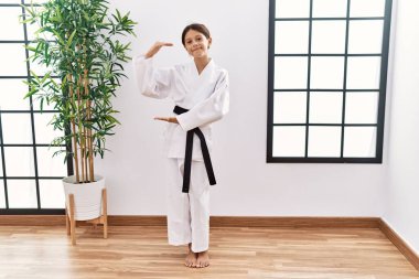Genç İspanyol kız karate kimonosu ve siyah kuşak giyiyor. Ellerinde büyük ve büyük boy işareti var. Ölçüm sembolü. Kameraya bakıp gülümsüyor. ölçüm kavramı. 