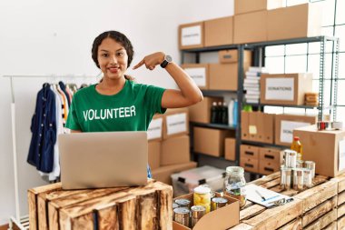 Güzel İspanyol kadın gönüllü tişört giyiyor. Dizüstü bilgisayarla çalışıyor. Gülümseyen mutlu ve gururlu birini işaret ediyor. 