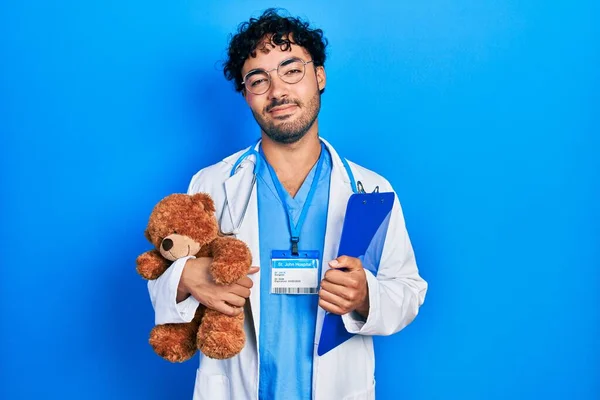 Młody Latynos Mundurze Doktora Trzymający Pluszowego Misia Schowek Zrelaksowany Poważnym — Zdjęcie stockowe