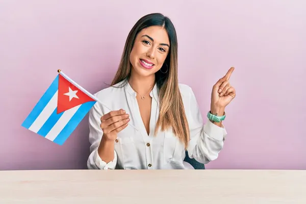 若いですヒスパニック女性保持キューバの旗上に座って笑顔幸せなポインティングとともに手と指で側面 — ストック写真