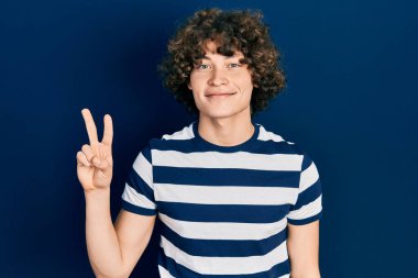 Yakışıklı genç adam rahat çizgili tişört giyiyor. İki numarayı gösterip işaret ediyor. Kendinden emin ve mutlu bir şekilde gülümsüyor.. 