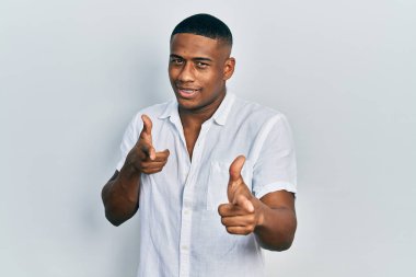 Gündelik beyaz gömlekli genç bir adam mutlu ve komik yüzüyle kamerayı işaret ediyor. iyi enerji ve titreşimler. 