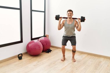 Genç İspanyol adam spor merkezinde halterleri kullanarak kendine güvenen bir şekilde gülümsüyor.