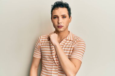 Makyaj yapan yakışıklı, rahat gömlekli, eli açık, dur işareti yapan, ciddi ve kendinden emin ifadeli, savunma jesti. 