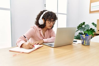 Ortadoğulu genç iş kadını kulaklık ve dizüstü bilgisayar kullanarak ofiste çalışıyor..