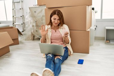 Orta yaşlı, beyaz bir kadın yeni evinde yerde otururken bilgisayarla video görüşmesi yapıyor..