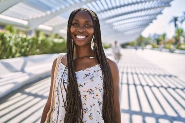 Genç Afrikalı Amerikalı kadın gülümseyerek şehirde mutlu mesut duruyor..