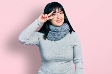 Genç İspanyol asıllı, uzun boylu, kış eşarbı takan, barış sembolü takan, yüzünde parmakları olan, neşeyle gülümseyen, zaferi gösteren bir kadın. 