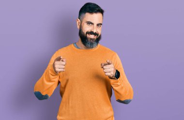 Kış süveteri giymiş sakallı İspanyol bir adam mutlu ve komik yüzüyle kamerayı işaret ediyor. iyi enerji ve titreşimler. 