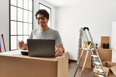 Genç İspanyol adam yeni evinde dizüstü bilgisayar kullanarak ekonomiyi hesaplıyor..