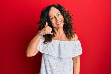 Orta yaşlı İspanyol kadın, günlük kıyafetler giyip gülümsüyor telefonla el ve parmak hareketleri yapıyor telefonda konuşuyor gibi. iletişim kavramları. 