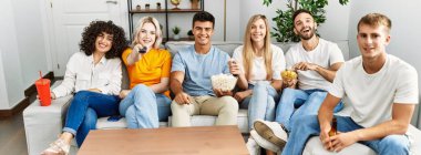 Mutlu bir şekilde gülümseyen bir grup genç arkadaş evde film izliyor..