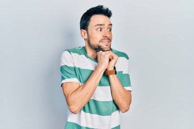 Gündelik kıyafetler giyen genç İspanyol adam gergin ve heyecanlı, elleri çenesinde yan tarafa bakıyor. 