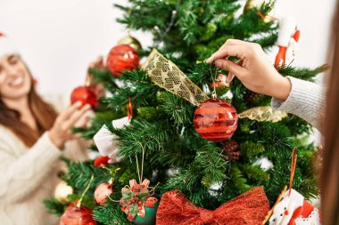 Evde kendine güveni olan iki kadın Noel ağacını süslüyor.