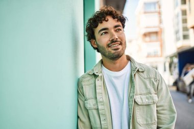 Yakışıklı, sakallı, güneşli bir günde mutlu bir şekilde gülümseyen bir İspanyol. Duvara yaslanmış.