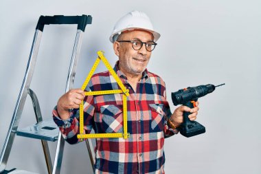 Yakışıklı, elinde tornavida tutan, inşaat merdivenlerinde kasket takan, gülümseyen ve kafasını çeviren yakışıklı bir adam.. 