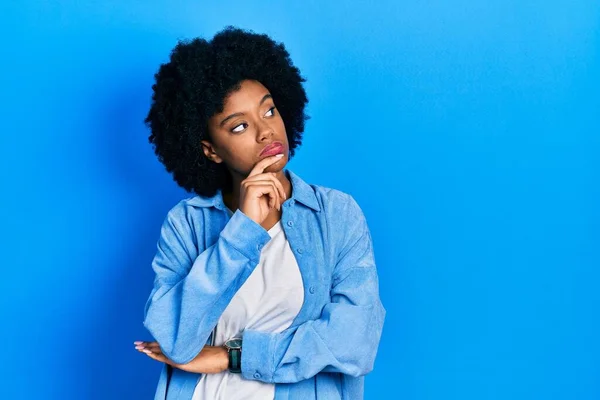 年轻的非洲裔美国女人穿着休闲装 双手托着下巴思考着问题 沉思着自己的表情 脸上挂着沉思的笑容 怀疑概念 — 图库照片