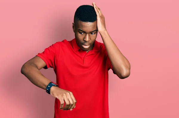 若いアフリカ系アメリカ人の男性は 心配時計の時間を見てカジュアルな赤のTシャツを着て 遅くなるのを恐れて — ストック写真
