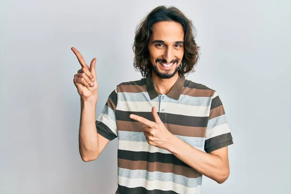 カジュアルな服を身に着けている若いヒスパニック系の男は笑顔とカメラを見て2本の手と指で側面を指して — ストック写真