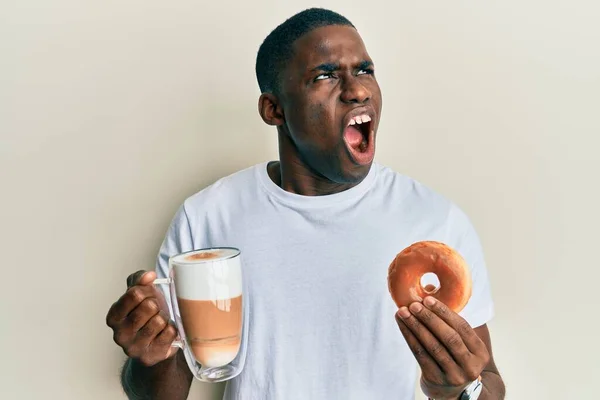 Νεαρός Αφροαμερικάνος Τρώει Ντόνατ Και Πίνει Καφέ Θυμωμένος Και Τρελός — Φωτογραφία Αρχείου