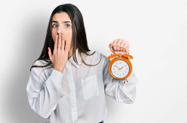 Young Brunette Teenager Holding Alarm Clock Covering Mouth Hand Shocked — Foto Stock