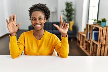 Genç Afro-Amerikalı kadın, gündelik giysiler içinde evdeki masada oturuyor ve yedinci parmaklarını göstererek gülümsüyor ve mutlu.. 