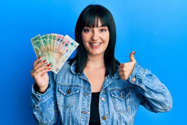 Birleşik Arap Emirlikleri 'ni elinde tutan genç İspanyol kadın gülümseyen ve olumlu gülümseyen dirhem banknotlar mükemmel ve onay işareti yapıyor. 