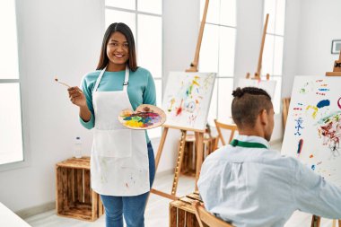 Resim stüdyosunda gülümseyen genç Latin ressam çift.