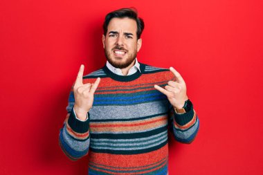 Sakallı, zarif yün kazak giyen, çılgın bir ifadeyle bağıran yakışıklı beyaz adam elleri havada rock sembolü yapıyor. Müzik yıldızı. ağır kavram. 