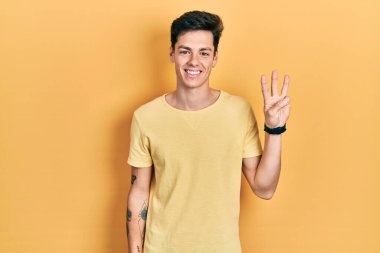 Gündelik sarı tişört giyen İspanyol genç adam üç numarayı gösterip işaret ederken kendinden emin ve mutlu bir şekilde gülümsüyor.. 