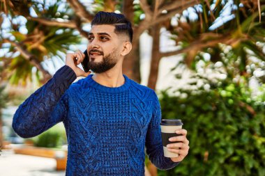 Genç Arap adam akıllı telefondan konuşuyor parkta kahve içiyor.