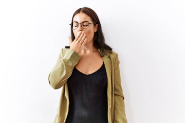 Genç esmer kadın izole edilmiş arka planda dikiliyor. Elle ağzını kapatmaktan sıkılmış. Huzursuz ve uykulu.. 