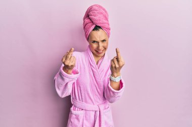 Young blonde woman wearing shower towel cap and bathrobe showing middle finger doing fuck you bad expression, provocation and rude attitude. screaming excited 