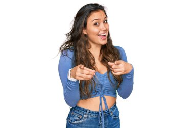 Günlük kıyafetler giyen genç İspanyol kız mutlu ve komik yüzüyle kamerayı işaret ediyor. iyi enerji ve titreşimler. 