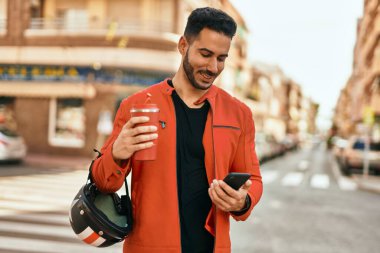 Genç İspanyol adam akıllı telefon kullanıyor. Şehirde kahve kaskı içiyor..