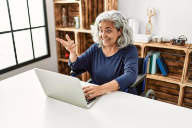 Orta yaşlı, gri saçlı, engelli bir kadın tekerlekli sandalyede otururken görüntülü konuşma yapıyor..