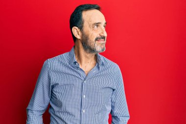 Orta yaşlı, sıradan kıyafetler giyen, yüzünde gülümsemeyle yan yana bakan İspanyol bir adam, doğal bir ifade. Kendinden emin gülen. 